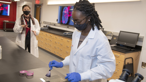Original Caption: (l. t. r.) From a safe distance Kimberlee Sue Moran, Associate Teaching Professor and Director of Forensics, Department of Chemistry  observes Sherifat Alaka (CAS '22) dust for fingerprints during special on-location work in the forensic