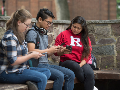 Rutgers students check their phones while sitting on the Red Lion Bench
