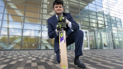 Deep Joshi in front of Rutgers Business School kneeling on the ground with a cricket bat