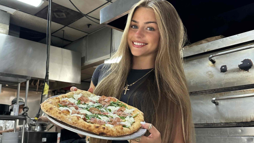 Woman in  a restaurant kitchen holding a pizza