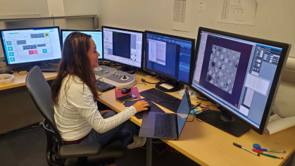 Woman sits before four computer screens examining images.