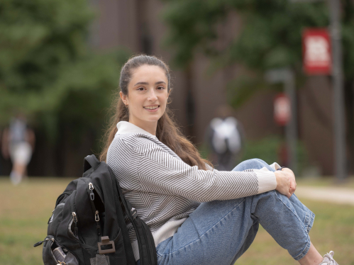 Amanda Casabona seated on the grass with her backpack on the Busch campus