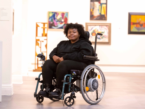 Raven Diaz seated in her wheelchair in front of an art exhibit at Zimmerli Art Museum