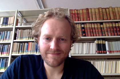 man in foreground with bookshelves containing books in background.