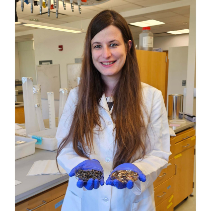 Scientist in lab coat and blue gloves holding superworms in each hand