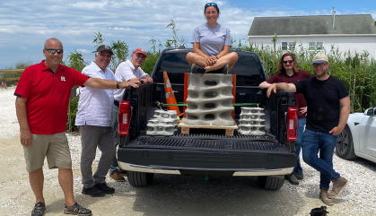 Group of people standing on a beach around a truck with a concrete structure in it.