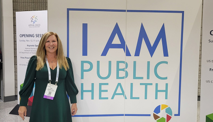 Lisa Gulla standing in front of a sign saying I'm Public Health